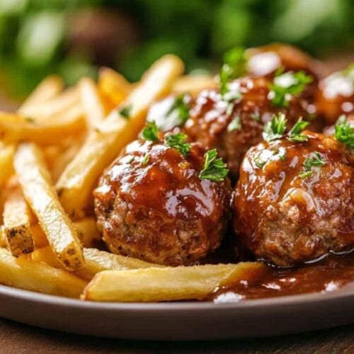 Boulette liégeoise servie avec des frites dorées, nappée de sauce brune, garnie de persil frais dans une assiette sur une table en bois.